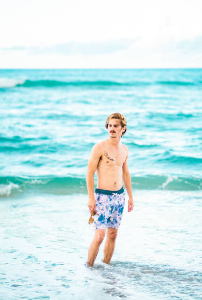 istock Handsome cool young gen z guy in swimsuit on the beach 1607769085