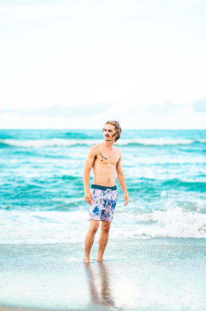 istock Handsome cool young gen z guy in swimsuit on the beach 1607769086