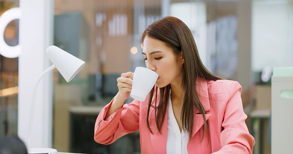 asian busy businesswoman is holding hot tea or coffee cup while working in office