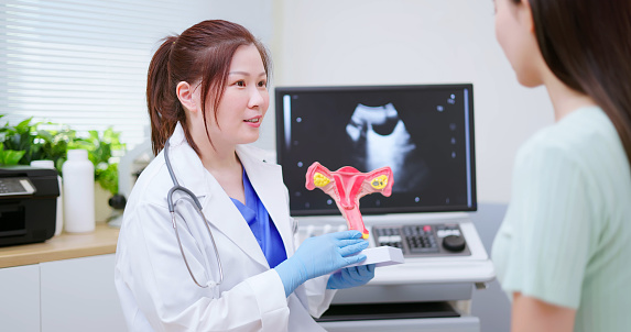 asian female doctor explaining uterus model to woman in hospital