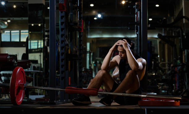 depressed athletic asian man after practicing routine weightlifting and overtraining at modern gym, active fitness people suffer pain injury accident from workout weight training in dark sport club hombre asiático atlético deprimido después de practicar levantamiento de pesas de rutina y sobreentrenamiento en un gimnasio moderno, las personas de fitness activo sufren lesiones por dolor accidente de entrenamiento con pesas en dark sport club