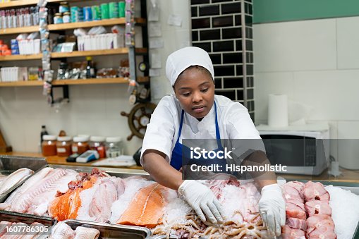 istock African-American woman working at a sea food market arranging the display of a variety of products on containers with ice 1607786305
