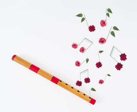 Creative layout made of wooden flute and musical notes made of various flowers on white background. Minimal musical instrument concept. Trendy wooden flute idea. Musical background aesthetic.
