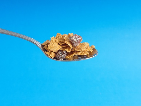 Overflowing spoon with morning breakfast cereal on blue background. High fiber raisin bran type cereal in spoon on sky colored background.