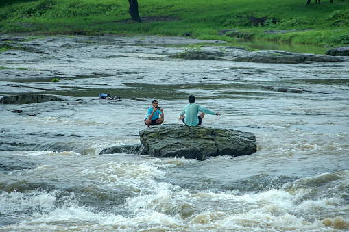 Pune, India - July 30 2023: Two young men in the middle of Indrayani river at Talegaon near Pune India. One posing and the other clicking his photo.
