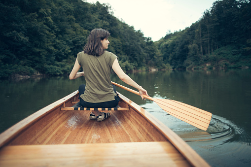 Rear view of woman paddling canoe on the lake, copy space.