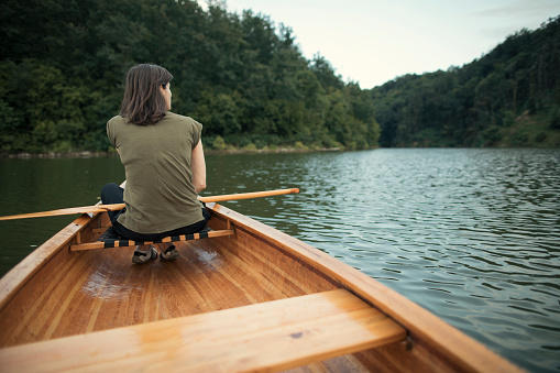 Rear view of woman paddling canoe on the lake, copy space.