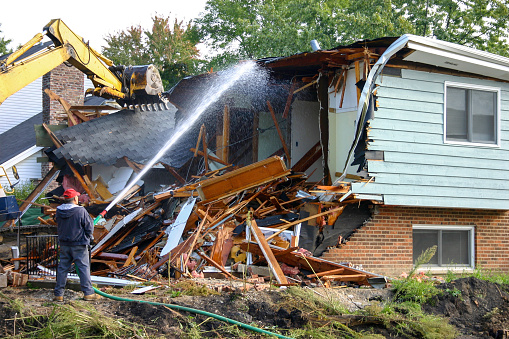 Arlington Heights, IL, USA - September 16, 2007: House being torn down. Construction worker is spraying water on building to keep dust down.