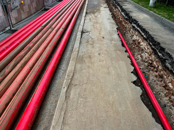 istock Red plastic pipes stacked on pavement and one pipe in a trench 1607849885