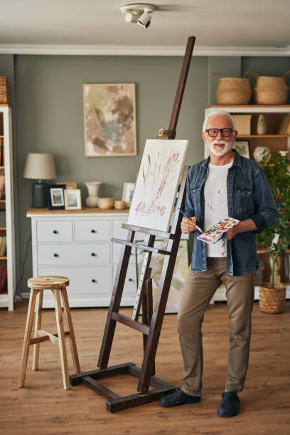 istock Elderly man painting on a canvas at home 1607857382