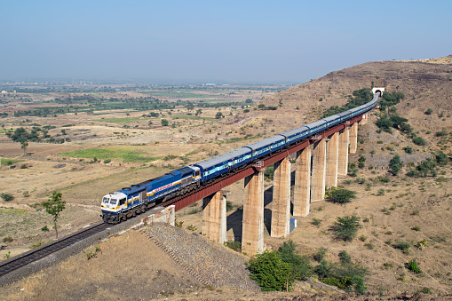 Shindawane, Maharashtra, India-December 26th, 2015:Indian railways long passenger train, exiting a tunnel to cross a tall railway bridge.
