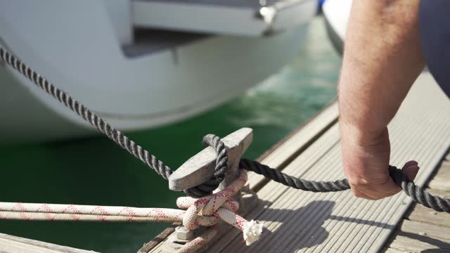 The sailor controls the position of the boat with the cleat hitch. Close-up of knot for cleat dock. Sailing boat. Mooring of a sailboat in the marina.4К