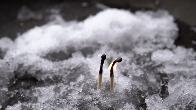 Two Matches are Burning in a Flame of Fire on Wet Snow. Close up