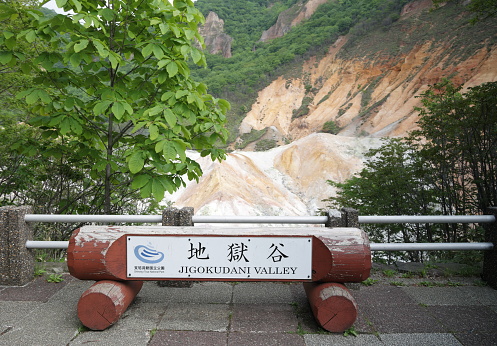 Noboribetsu Onsen, Japan - June 6, 2023: A sign for Jigokudani Valley welcomes resort visitors to Hell Valley. Background shows the volcanic crater and hot springs activity in Shikotsu-Toya National Park. Spring afternoon with overcast skies in Iburi Subprefecture, Hokkaido Prefecture.