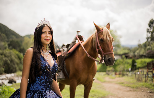 A beautiful young woman with a crown in her hair and a horse at her side in an open field.