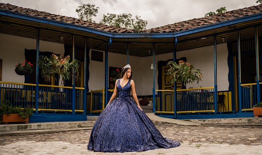 young woman in her quinceañera dress in the middle of a typical colombian house looking to the side with a tiara in her hair