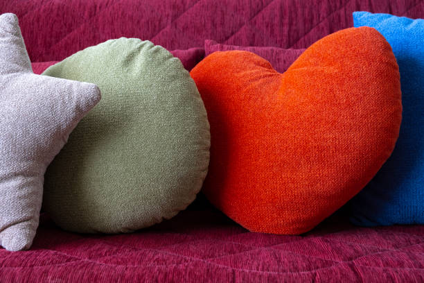 istock Decor Pillows composition on a couch sofa in modern apartment, home interior. Designed various shapes forms and colors pillows, orange heart, grey star, blue square, green circle. Closeup of comfortable pillows decoration on sofa in living room 1607993908