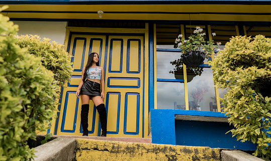 beautiful young woman with long hair standing in the doorway of a typical colombian house