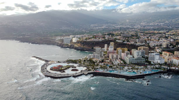 Aerial View of Puerto de la Cruz Bay Captured from the skies above, this breathtaking aerial shot showcases the vibrant cityscape of Puerto de la Cruz. The drone's perspective reveals the intricate layout of the city, nestled beautifully alongside the serene bay. puerto de la cruz tenerife stock pictures, royalty-free photos & images