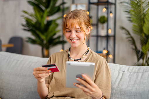 Young woman shopping online using digital tablet and a credit card at home.