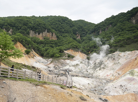 Resort visitors go along an elevated boardwalk to the Observation Deck in Jigokudani, Hell Valley. Gases escape from the many fumaroles on the volcanic crater. Spring afternoon in Iburi Subprefecture.
