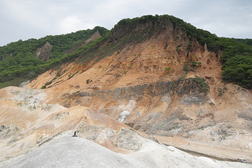 Gases escape from fumaroles on the volcanic crater in Noboribetsu Onsen in Shikotsu-Toya National Park. Spring afternoon with clouds in Iburi Prefecture.