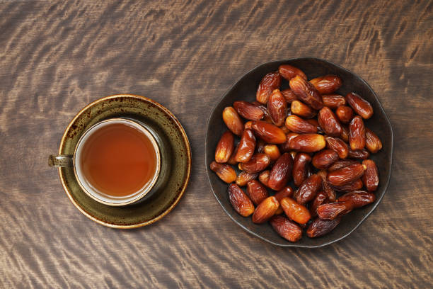 Dried dates in a plate and a cup of tea on a wooden background. Popular food for Ramadan. Top view, flat lay. Dried dates in a plate and a cup of tea on wooden background. Popular food for Ramadan. Top view, flat lay. jujube fruit stock pictures, royalty-free photos & images