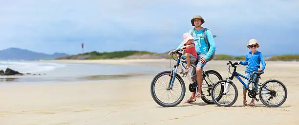 Father and kids riding bikes along a beach