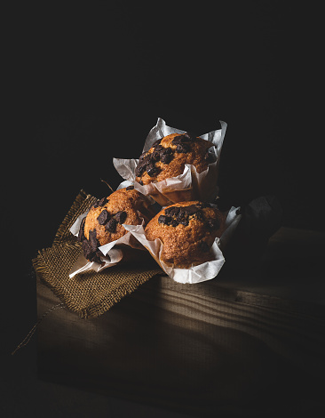 cupcakes with chocolate chips, on a wooden drawer, illuminated from the side, dark mood style