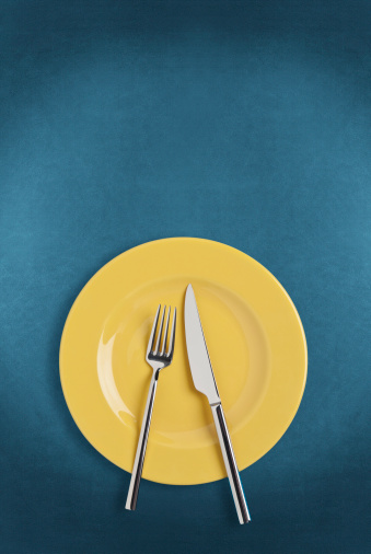 Empty yellow plate and fork,spoon and table knife isolated on blue background.