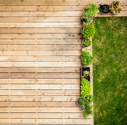 a wooden patio with flowerpots and a piece of lawn, viewed from above. this photo was taken during the 