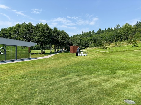 Glass modern golf club building and white golf balls lie in basket on green grass on sunny summer day. A place to play golf