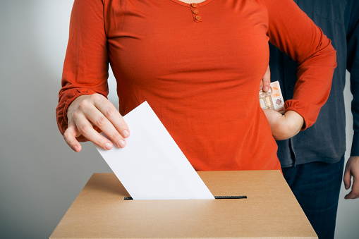 adult woman casting her vote while getting some cash (euros) from a guy standing behind her.