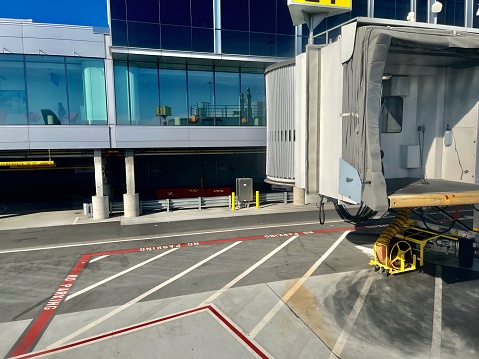 An airport jet bridge sits retracted and ready to connect the airport to a commercial airplane. Airport viewing windows are in the background.