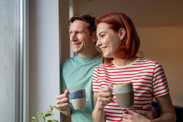 istock Smiling happy couple drinking coffee looking out window 1608252599