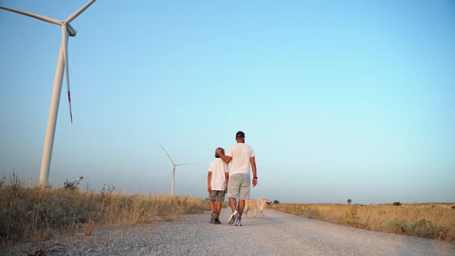 Happy Man Father Child Son boy Walking and pet golden retriever dog in a Wind farm. Enjoying time Together and Clean Air in a More Environmental Friendly Sustainable Efficient Energy Life