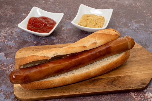 Hot Dog on a cutting board on a background of cups with ketchup and mustard