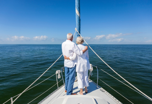 A happy senior couple embracing at the front or bow of a sail boat on a calm blue sea looking to an clear horizon