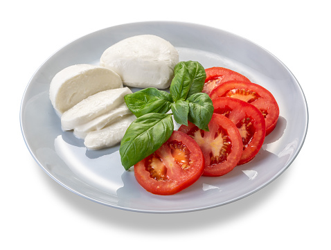 Caprese salad made with fresh sliced tomatoes, mozzarella and basil in plate isolated on white with clipping path included