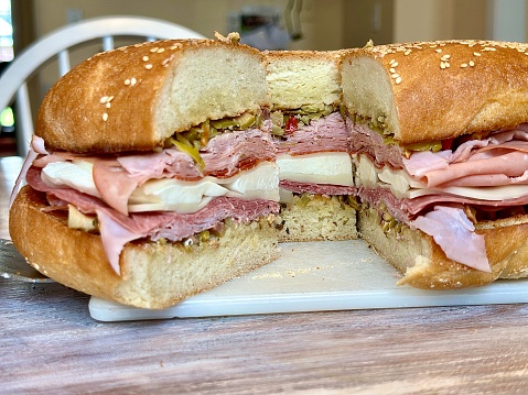 A giant muffuletta sandwich ready to be cut with a cleaver.