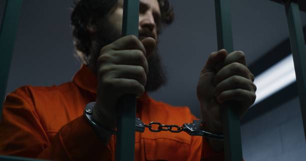 istock Prisoner in orange uniform and handcuffs holds metal bars 1608502966