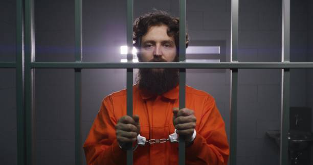 istock Prisoner stands in prison cell in handcuffs, looks at camera 1608510204