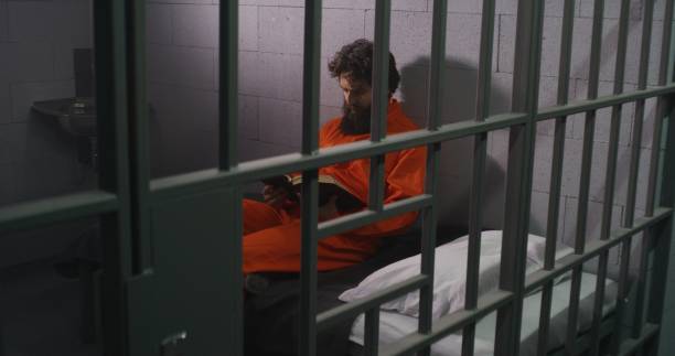istock Male prisoner sits on bed, reads Bible, prays 1608511893