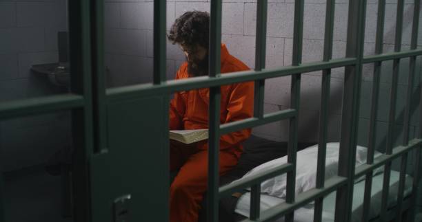 istock Male prisoner sits on bed, reads Bible, prays 1608513948