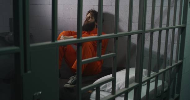 istock Male prisoner sits on bed, reads Bible, prays 1608516505
