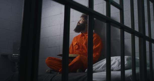 istock Male prisoner sits on bed, reads Bible, prays 1608526901