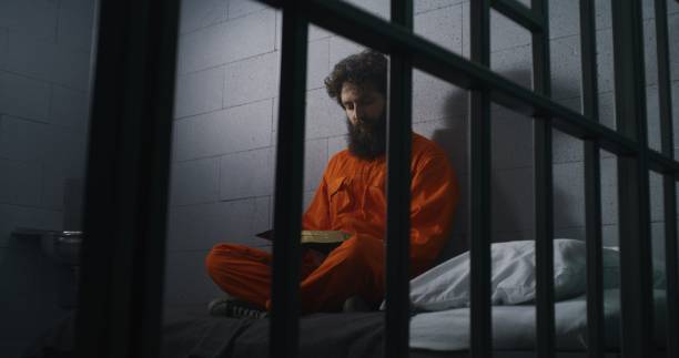 istock Male prisoner sits on bed, reads Bible, prays 1608527911