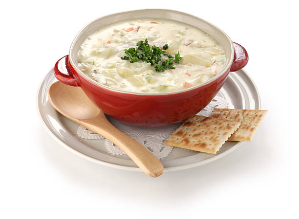 A bowl of clam chowder with a spoon and two saltine crackers