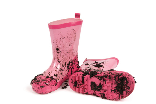 Pink gumboots covered in mud against a white background.