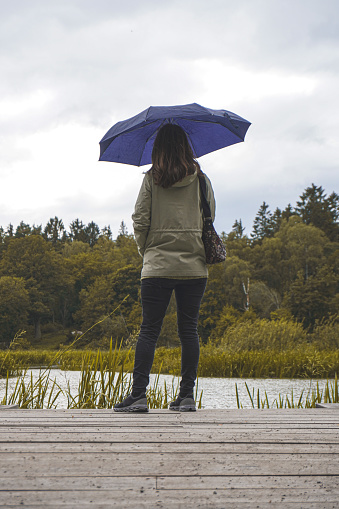 Rear view of woman with umbrella standing on pier against sky